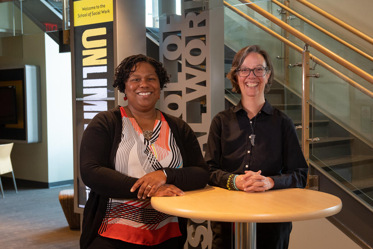 A photo of two women standing behind a small circular table. 