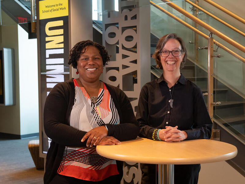 A photo of two women standing behind a small circular table. 