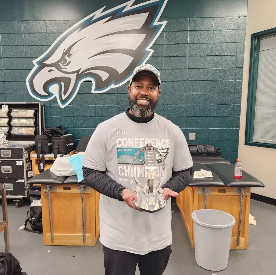 A man smiling while holding a glass trophy shaped like a football. 