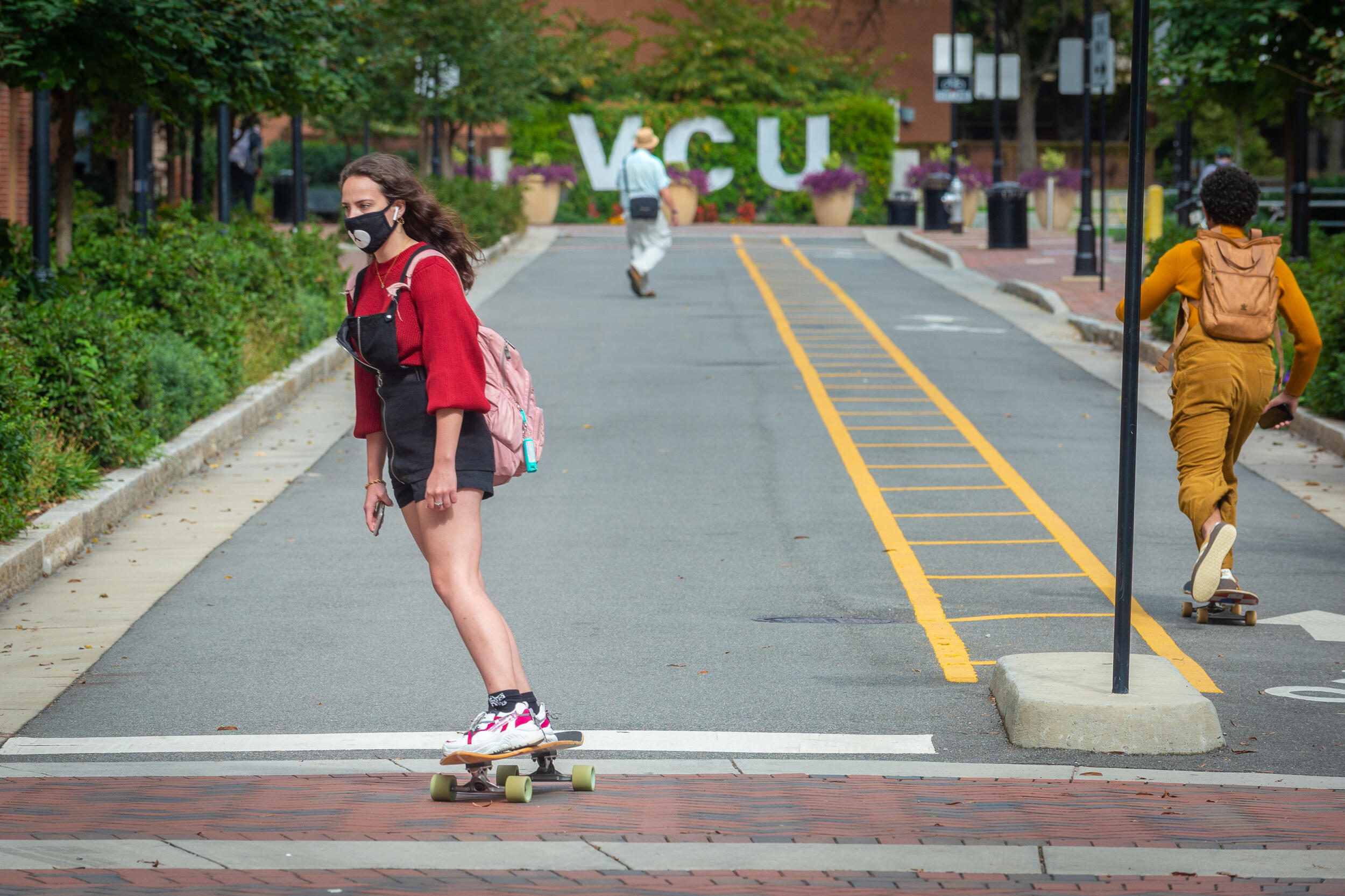 A student skateboards to class on a city street in front of a green wall with VCU letters on it.