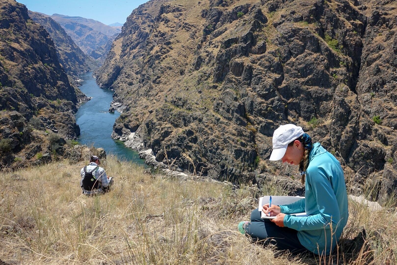 Two students seated on a bluff overlooking a river valley.
