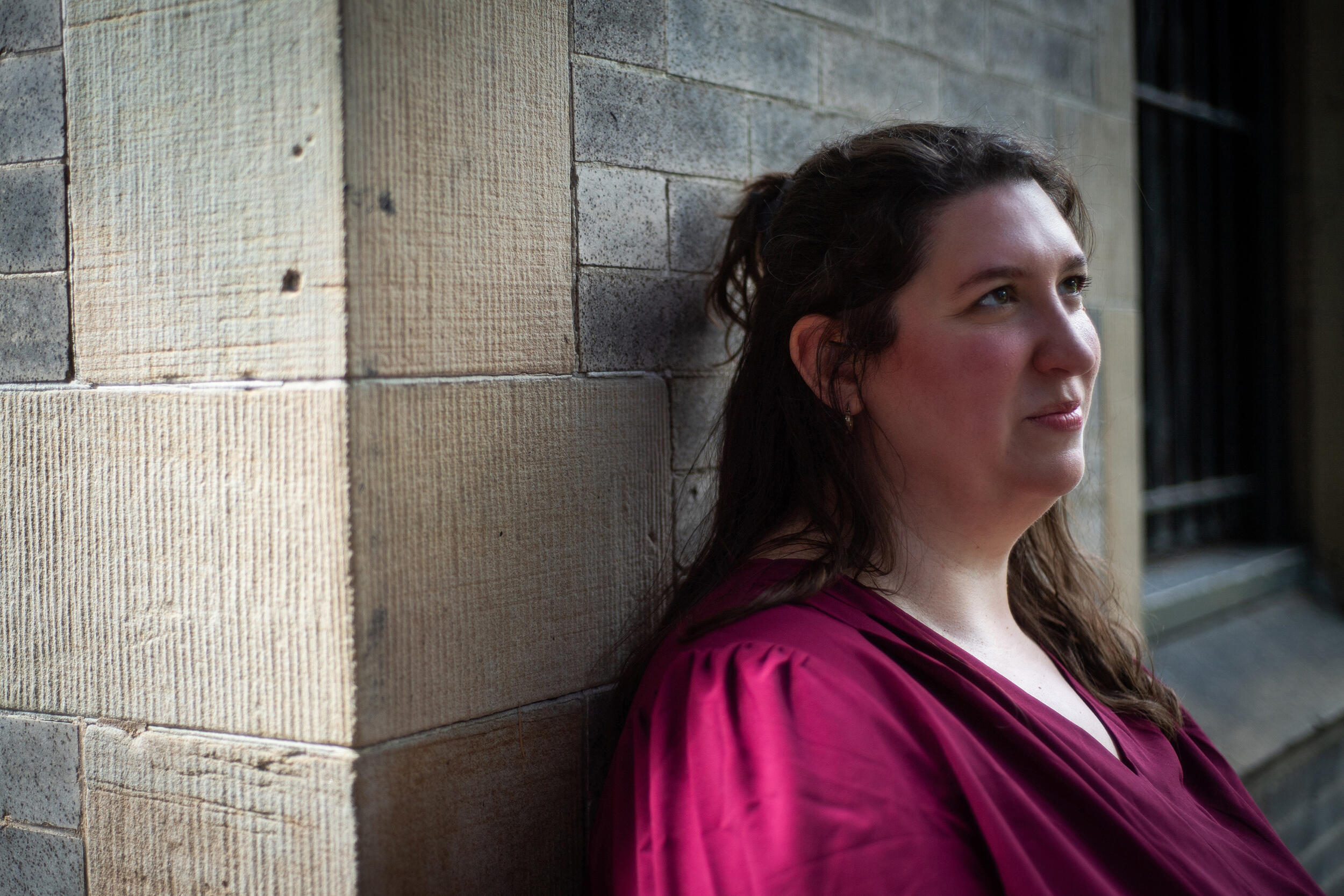 A photo of a woman standing against a wall from the shoulders up. 
