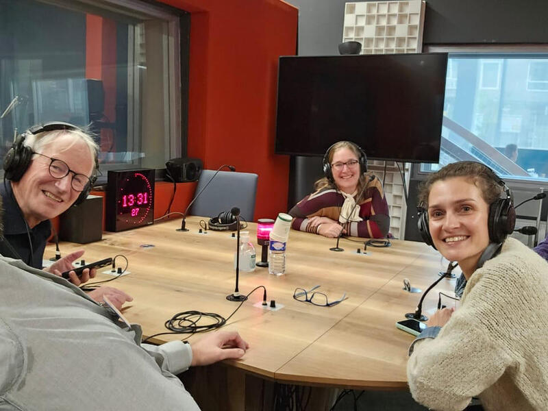 A photo of five people wearing headphones sitting around a table with small microphones on it. 
