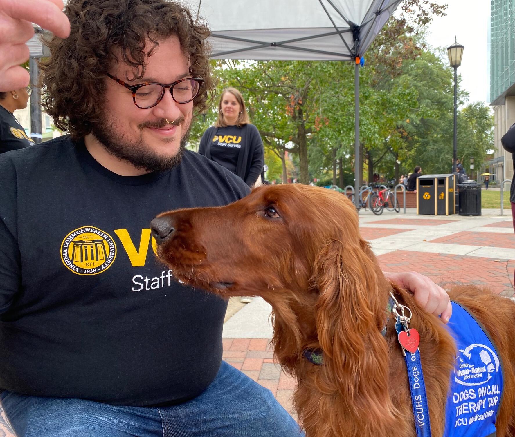 A man kneeling next to a dog wearing a blue vest 