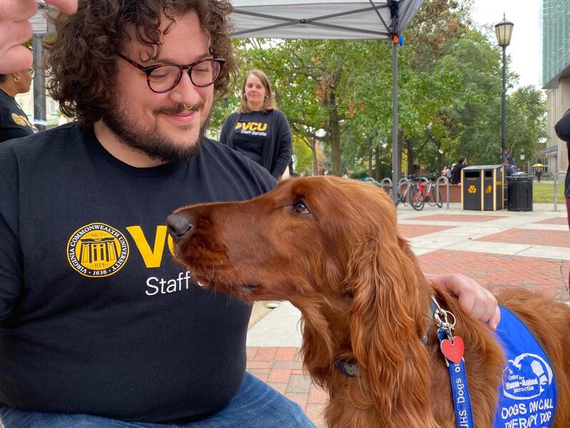 A man kneeling next to a dog wearing a blue vest 