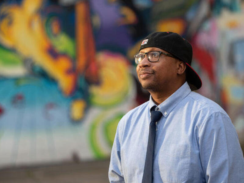 Marc Cheatham, wearing a backwards baseball cap, standing in front of a colorful mural in Richmond.