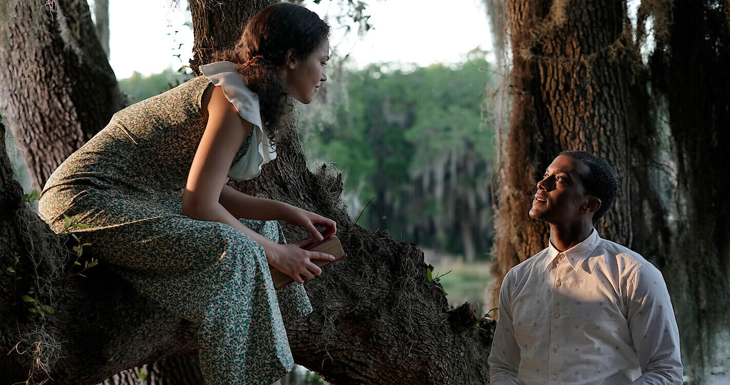 A woman sitting on a tree branch speaks to a man standing below her.