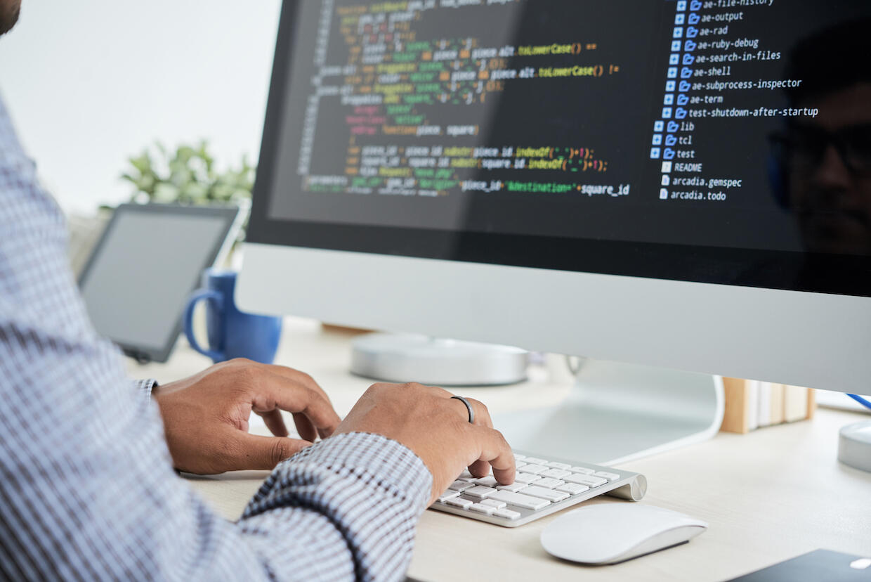 Man with checkered shirt using computer to type html code. 
