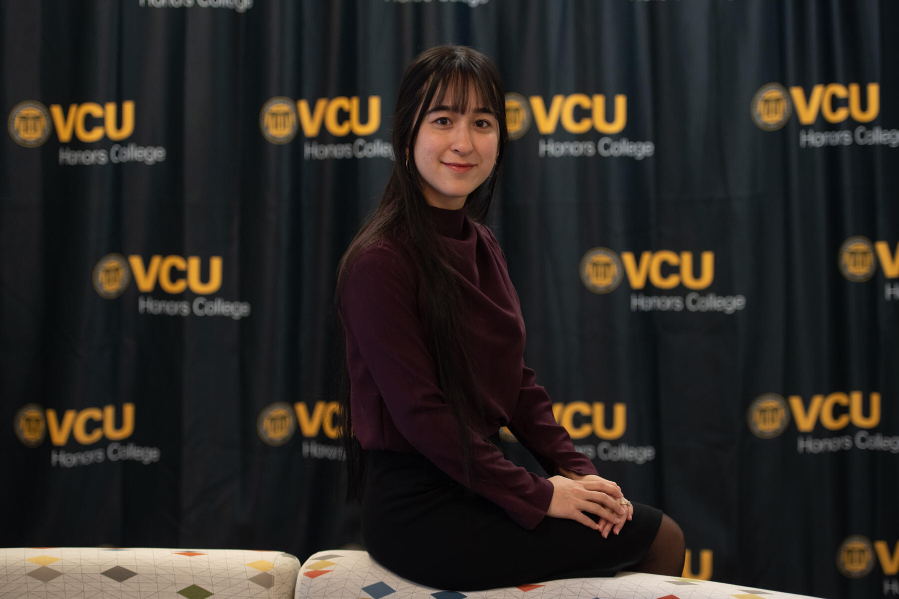 A photo of a woman sitting in front of a curtain covered in VCU logos