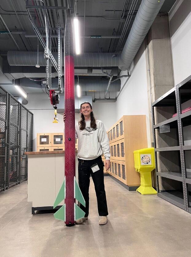 A photo of a man smiling and holding a rocket. 