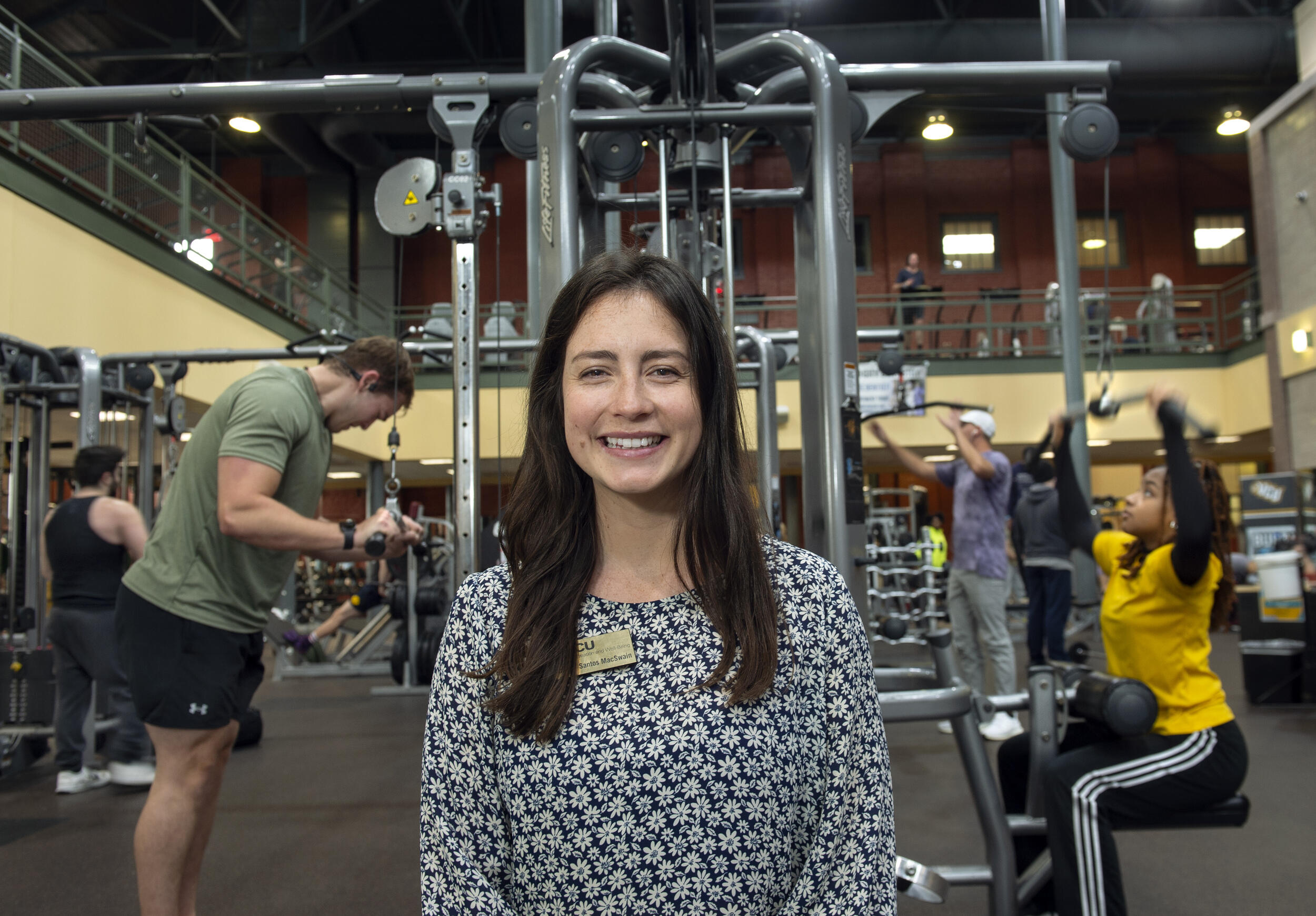 A woman smiling in a gym with people working out behind her