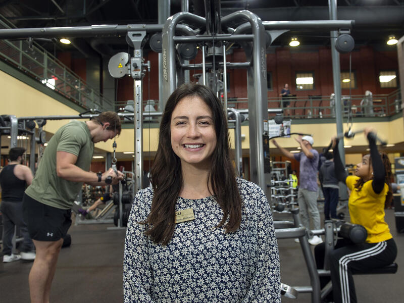 A woman smiling in a gym with people working out behind her