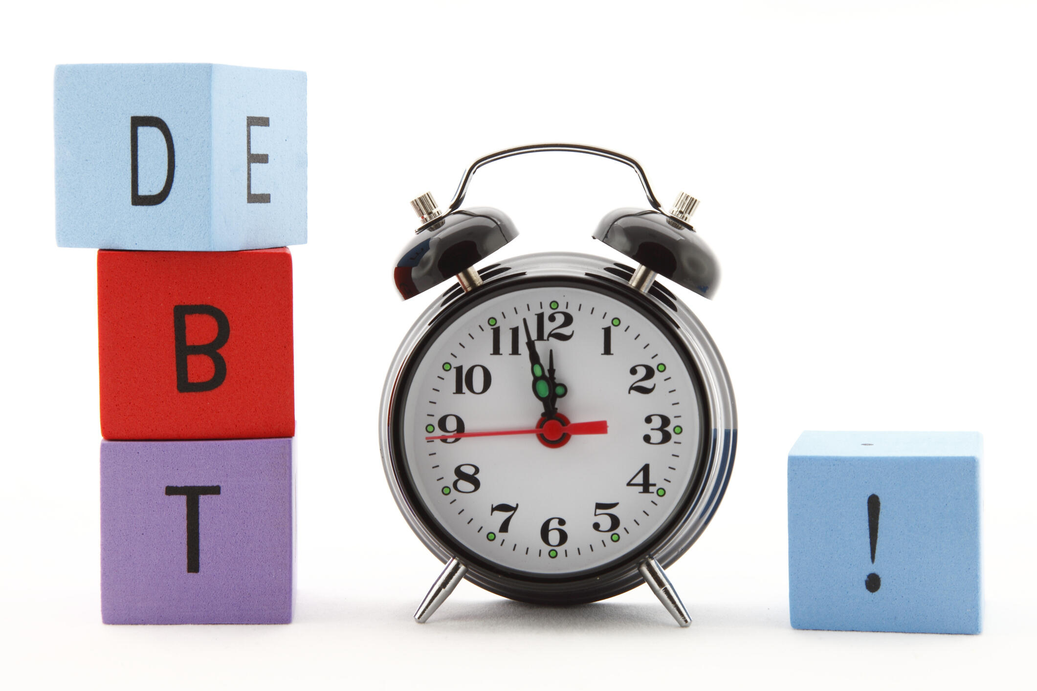 A photo of an alarm clock with multicolored building blocks on either side of it. The three blocks on the left side spell out \"D\" \"B\" \"T\" and the one on the right has an exclamation point on it.