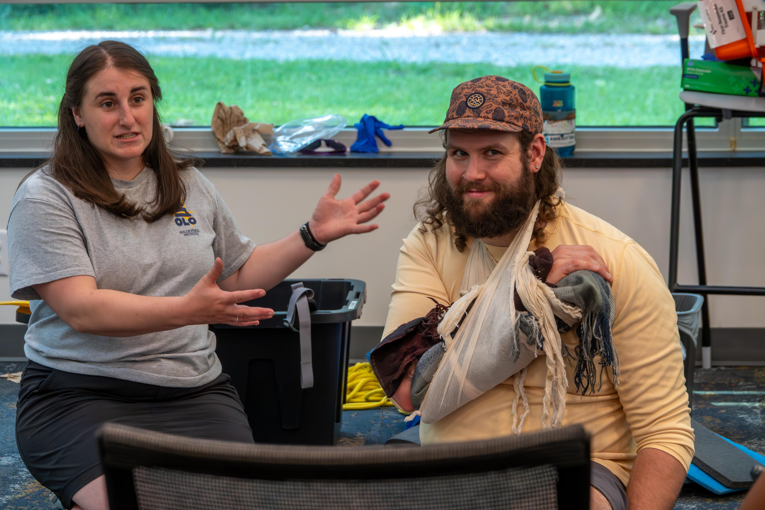 A photo of a woman gesturing to a man to her right who has on a makeshift sling. 