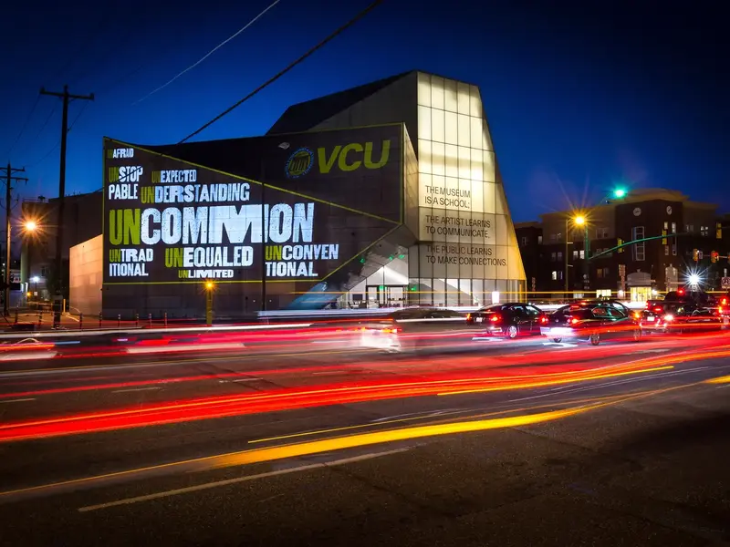 A long exposure image of cars passing by the Institute for Contemporary Art at VCU lit with a projection of an artistic rendering of a word cloud of words that represent the uncommon experience VCU offers: Unafraid, unlimited, understanding, unequaled, uncommon, unexpected, unstoppable and unconventional.