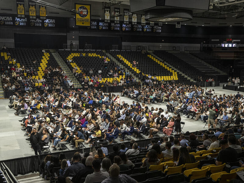 Photo of hundreds of people sitting in chairs at the VCU Siegel Center with the seats in the background spelling VCU.