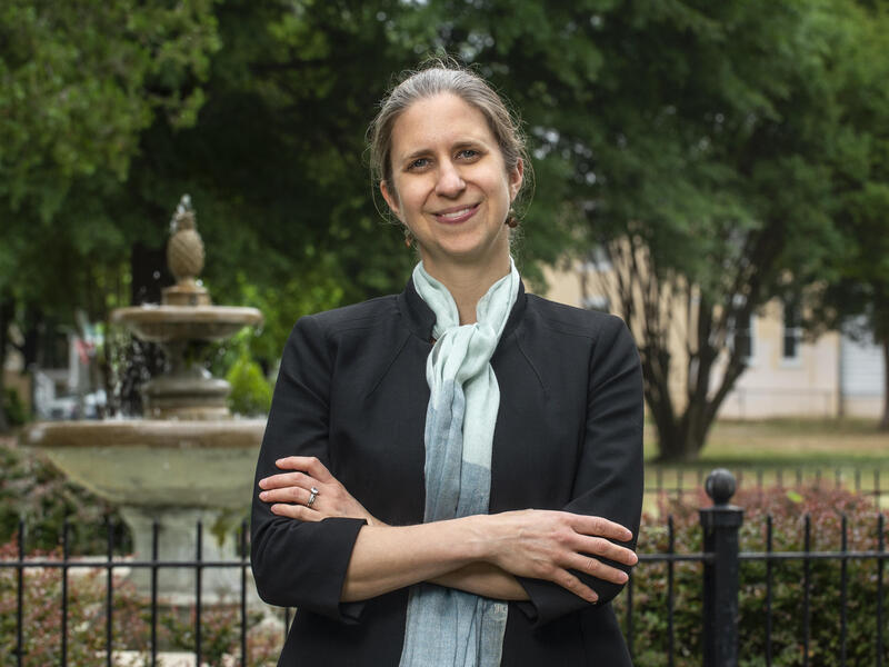 Woman stands with her hands folded in front of a fountain outdoors.