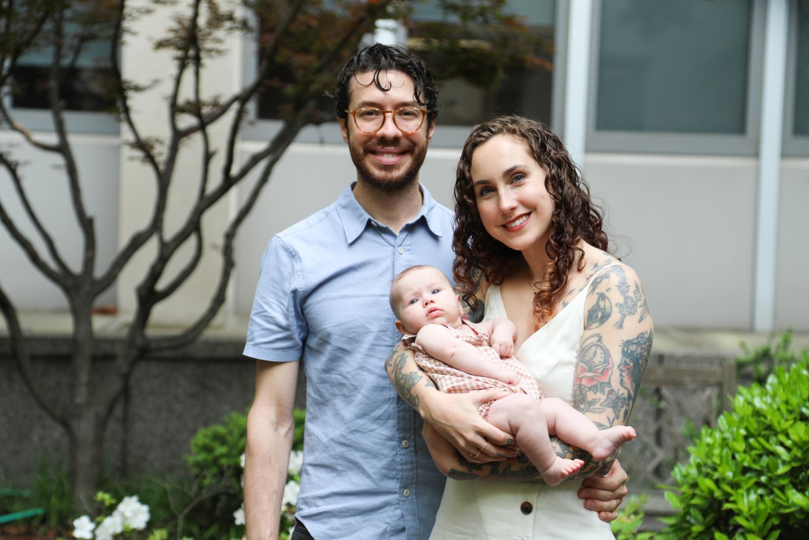 A photo of a man standing nexgt to a woman who is holding an infant. 