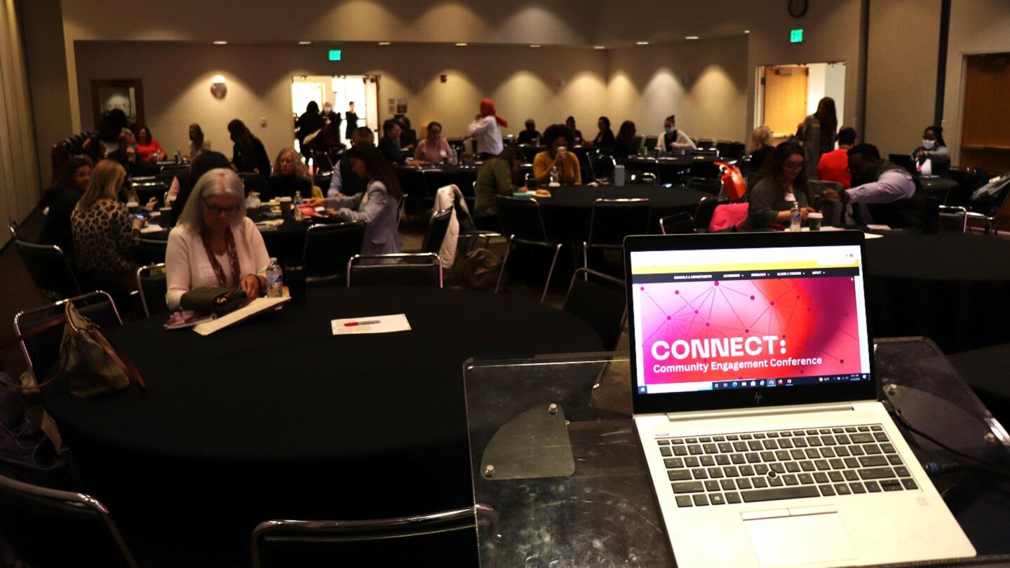 A photo of a laptop sitting on a podium in a room full of people. The screen of the computer says \"CONNECT.\" in white letters