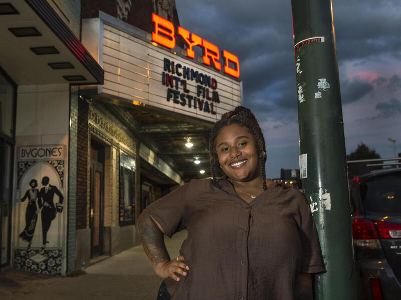 A photo of a woman standing in front of the Byrd Theater with her left hand on her hip. 