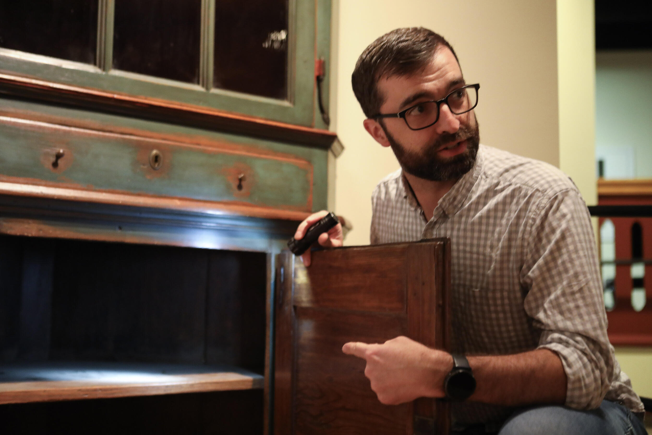 A photo of a man kneeling next to an old cupboard. 