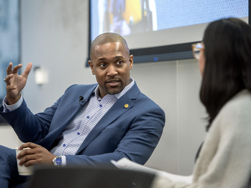 A photo of a man sittng and speaking to a woman to the right of him. 