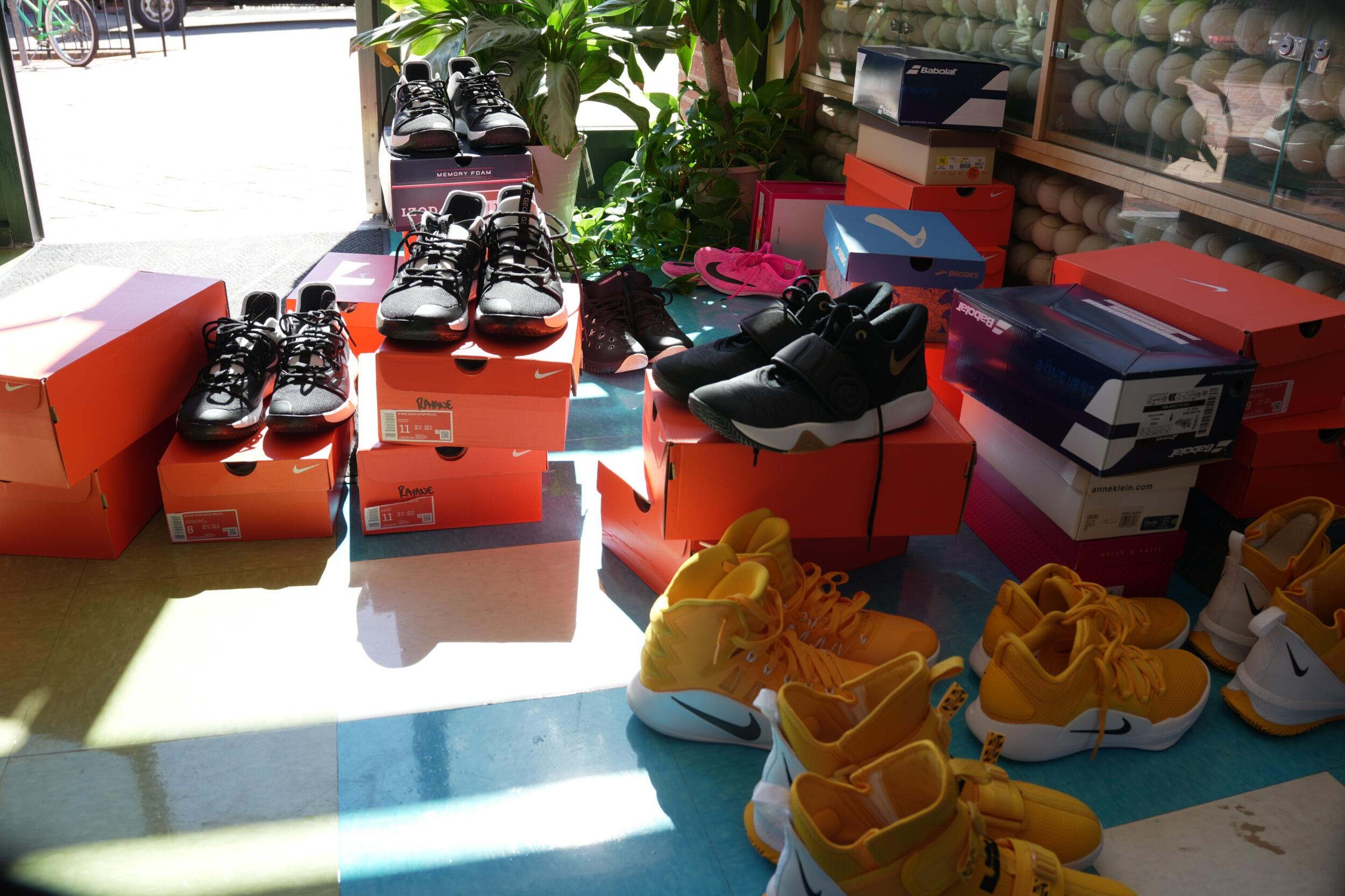 A photo of orange shoe boxes stacked on top of the floor. On top of and around the boxes are multiple pairs of sneakes. 
