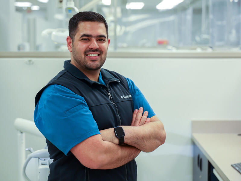 A man standing in a dental exam room with his arms crossed across his chest.