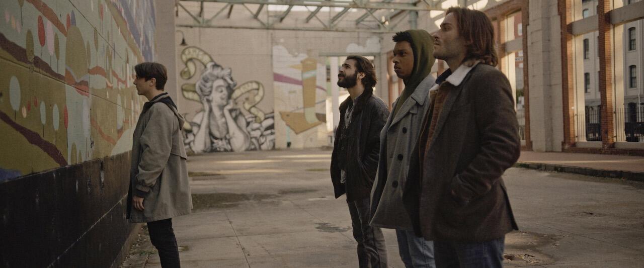 Still image from \"Welcome to the Show\" of four young men staring at a wall