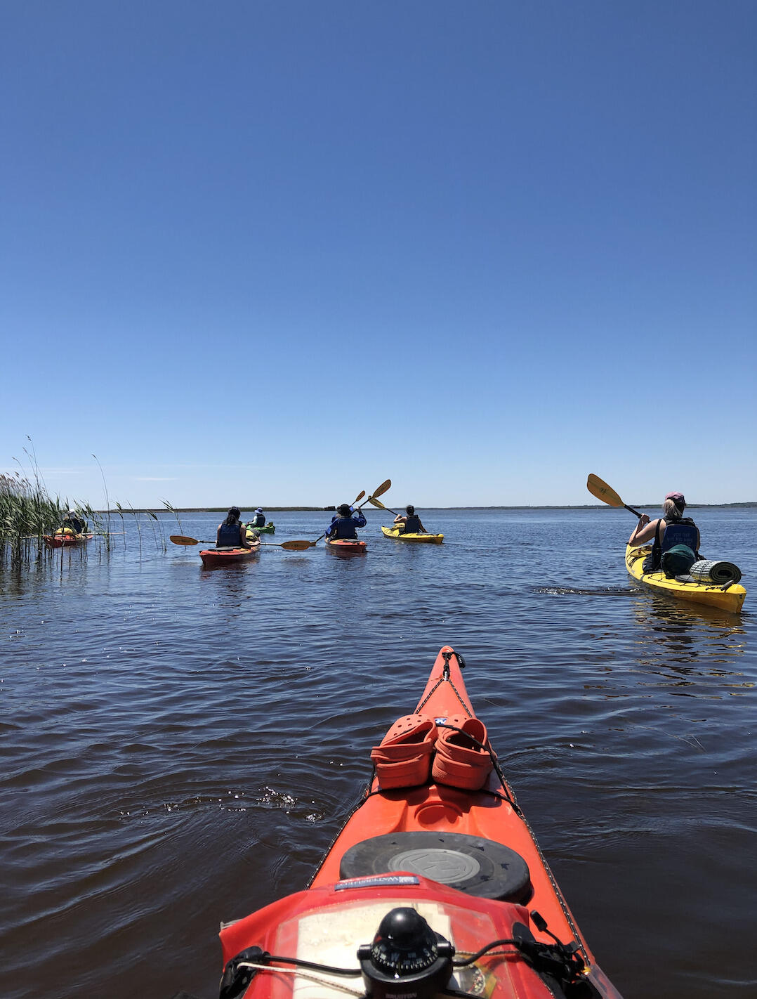 The front of a kayak looking out at a river and other people kayaking in front of it 