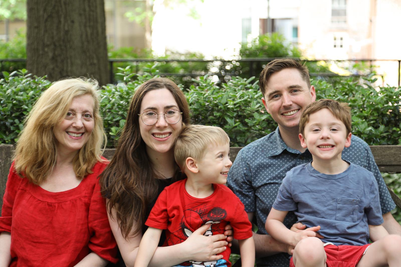 A photo of two women, one older and one younger, and a man sitting on a bench. The younger woman and man have two young boys sitting on their laps. 