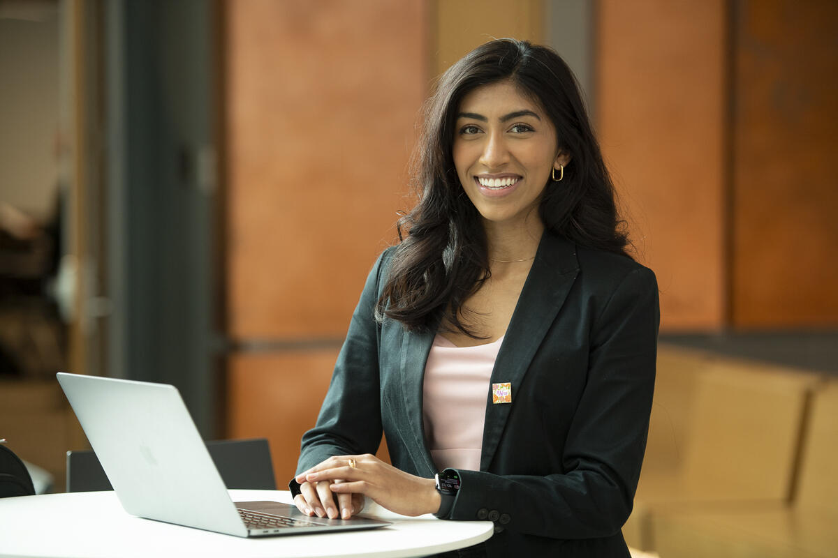 A woman wearing a black sports coat sitting at a table with a laptop in front of her. 
