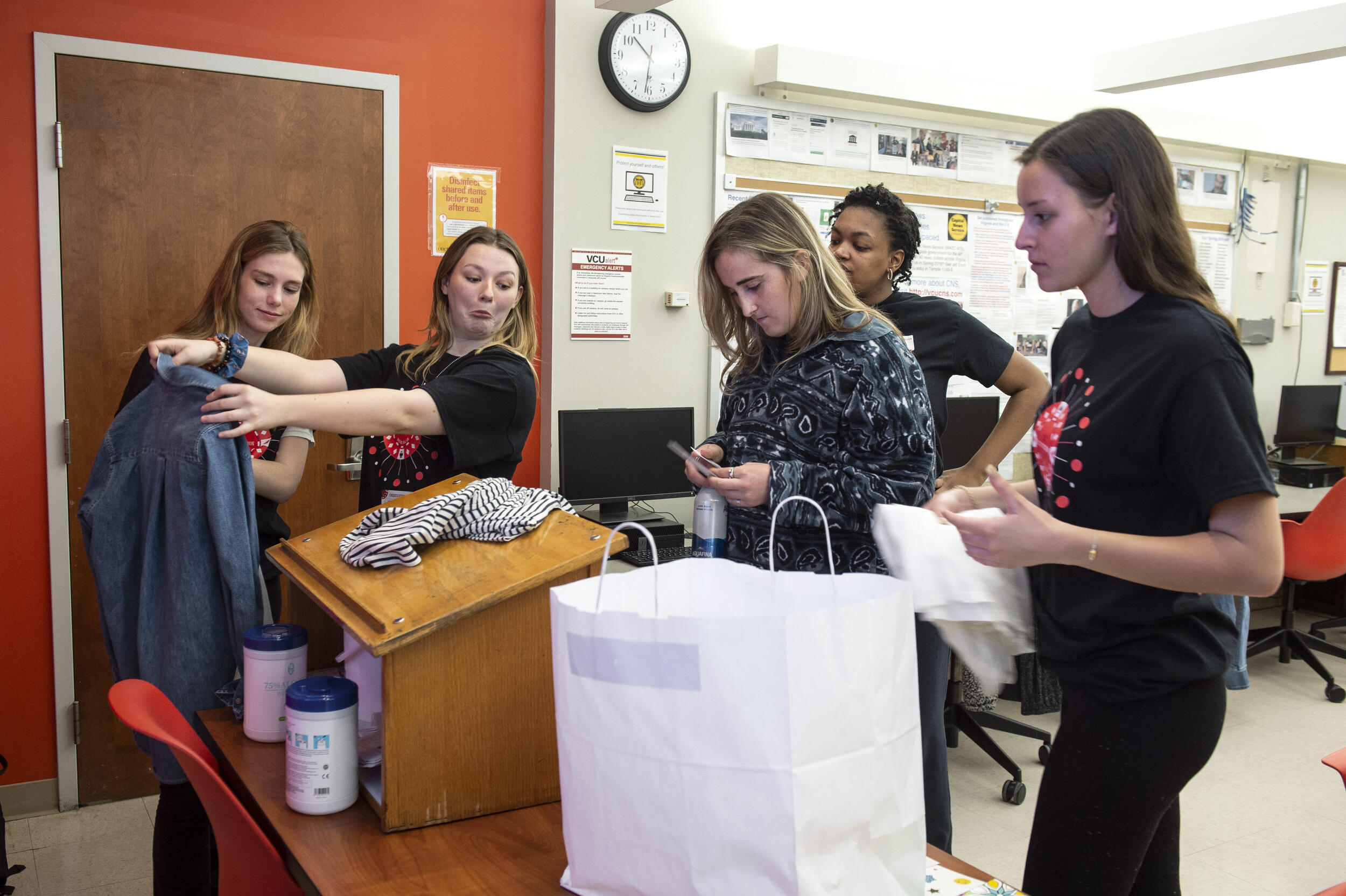 Students looking at cloths, one is holding a shirt with outstretched arms 
