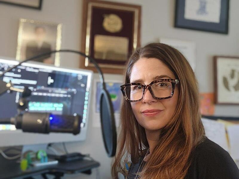 A photo of a woman sitting at a table with audio equipment. 