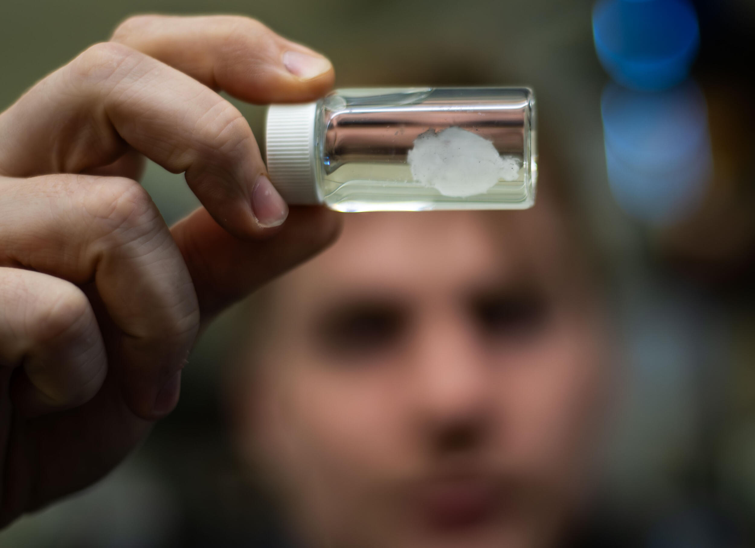A photo of a small model brain in a jar being held by a person. 