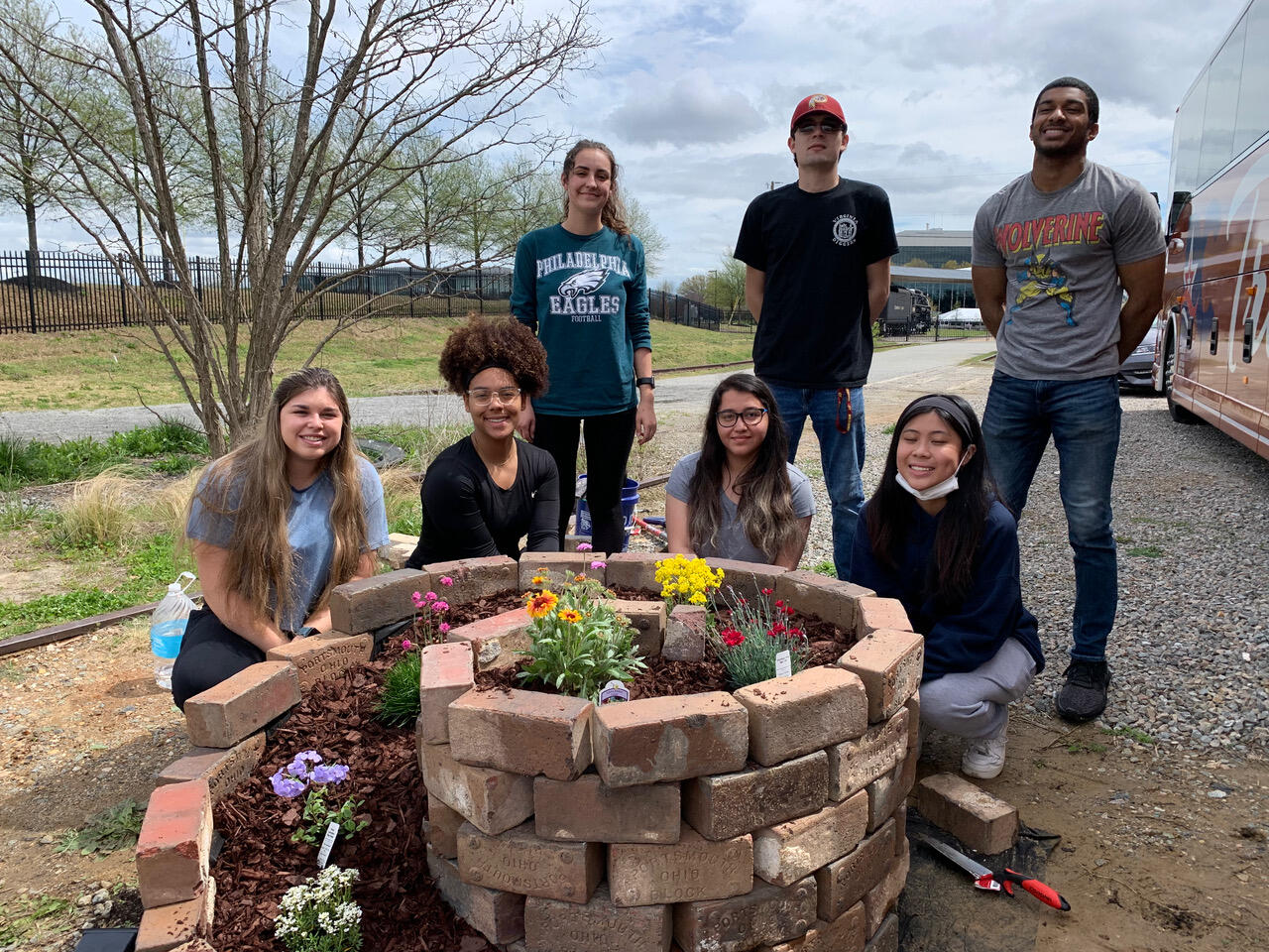Seven students standing around a flower planter made out of bricks 