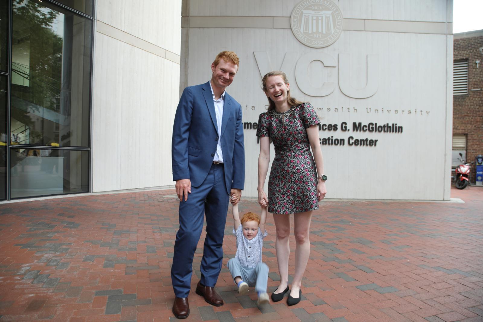 a man and woman holding the arms of a small child who is dangling near the ground. The woman is laughing. 