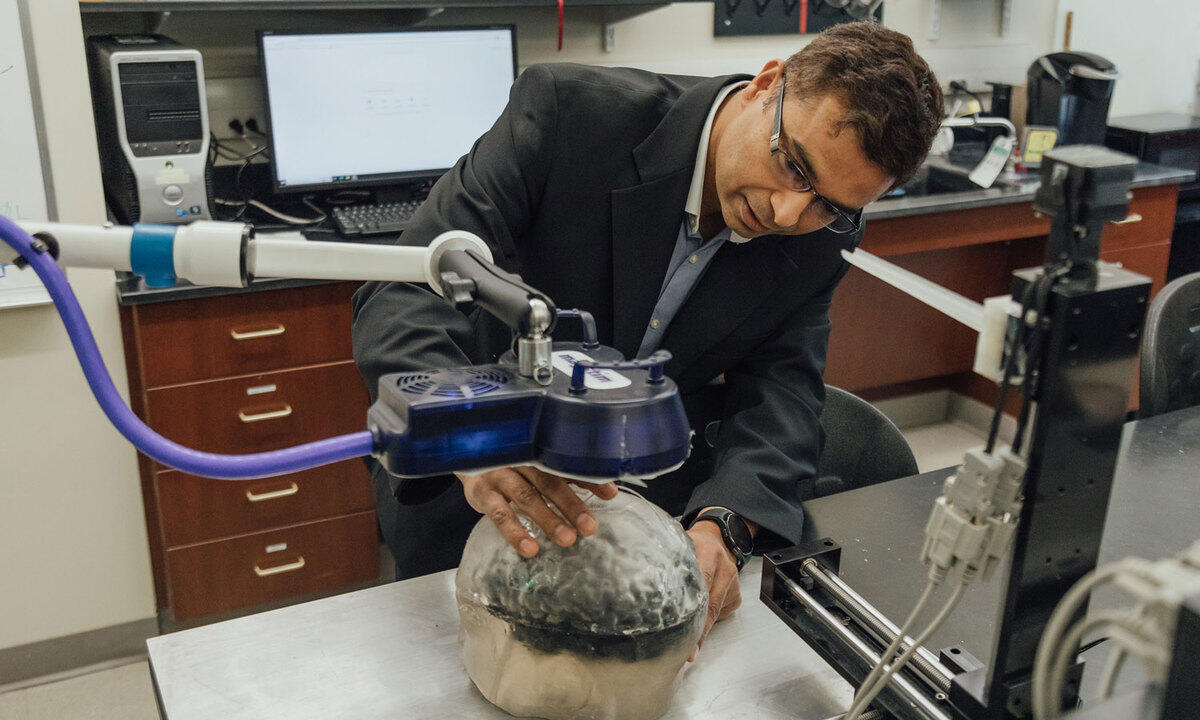 A man holding a model of a human brain under a piece of physics equipment 