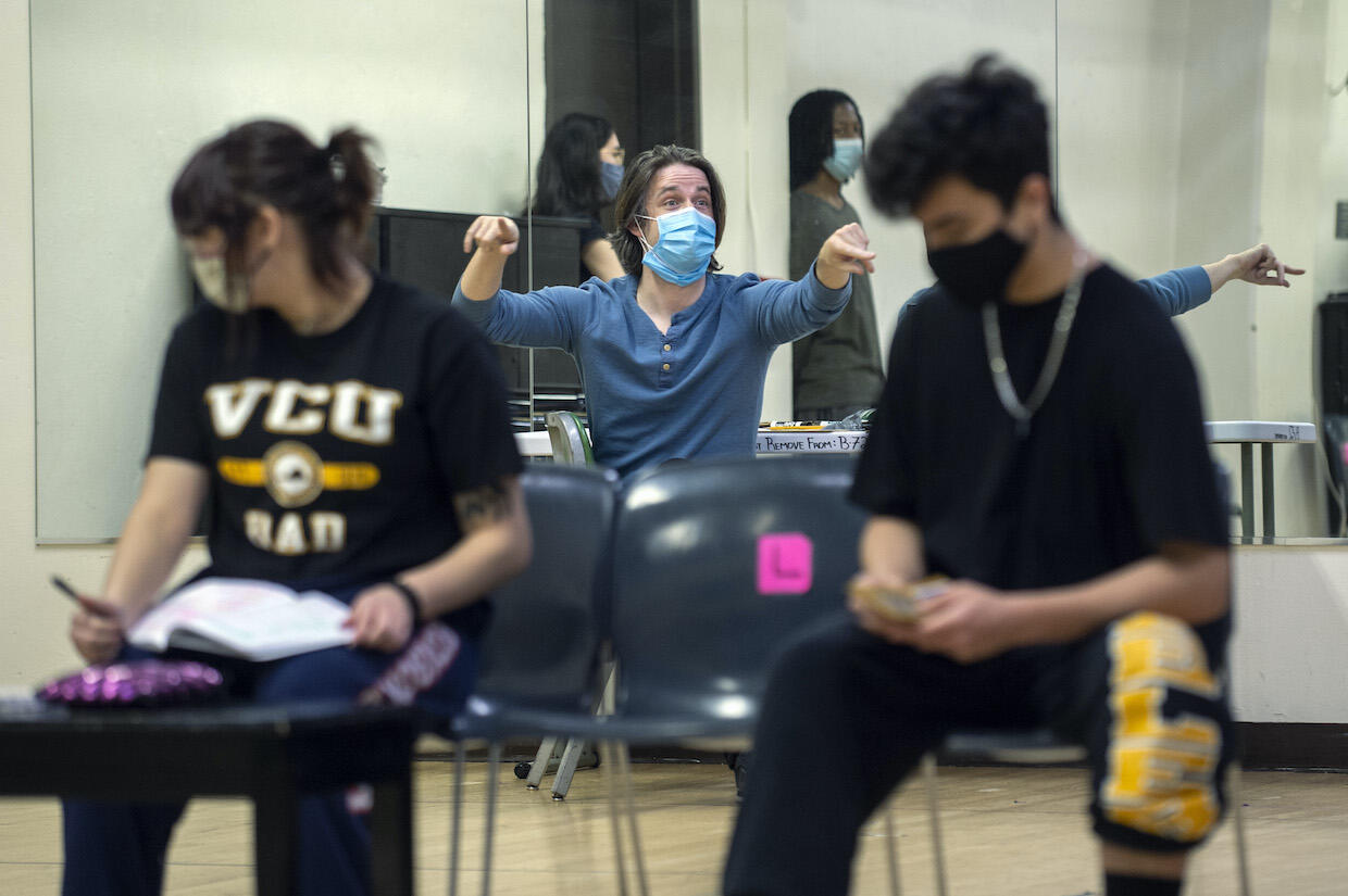 A professor guides students in the background. Two students sit in the foreground.