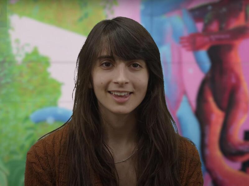 A photo of a woman from the chest up in front of a mural. 