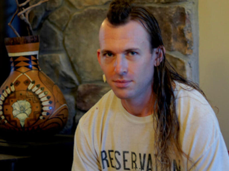 A portrait of a man with a long mohawk sitting next to a vase 
