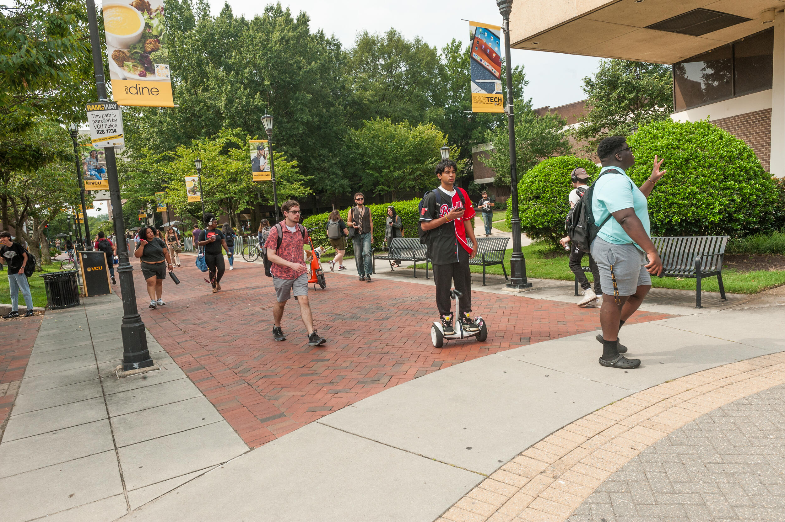 People walking along a sidewalk and one person riding a hover board. 