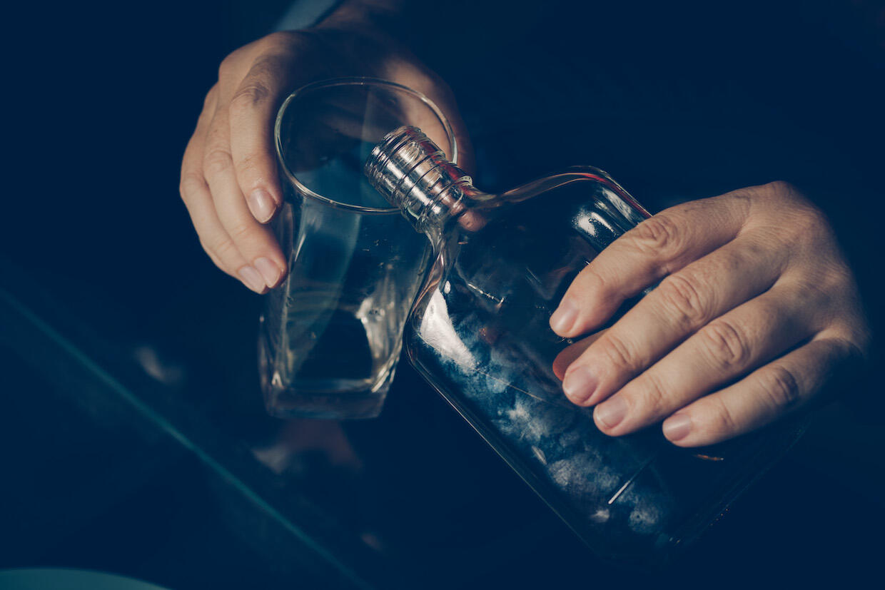 A person pours a drink from a glass bottle.