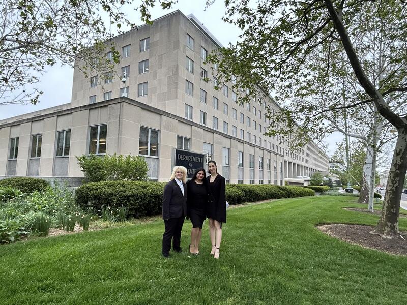 A photo of three students standing on the grass in front of the Department of the State building in Washington D.C. 