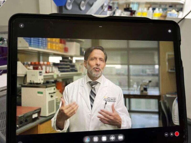 A man in a white doctor's coat and tie talking on a screen