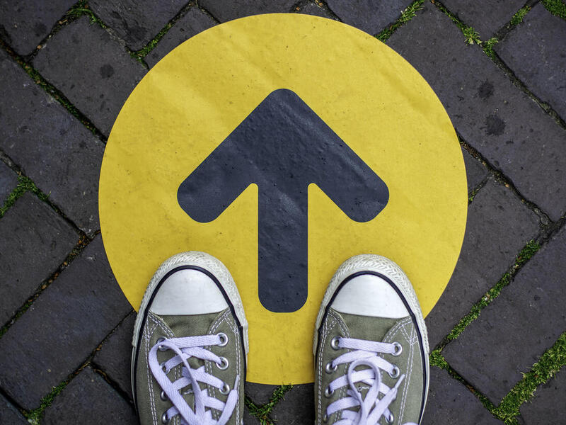 A pair of shoes standing on a dot with an arrow pointing forward.