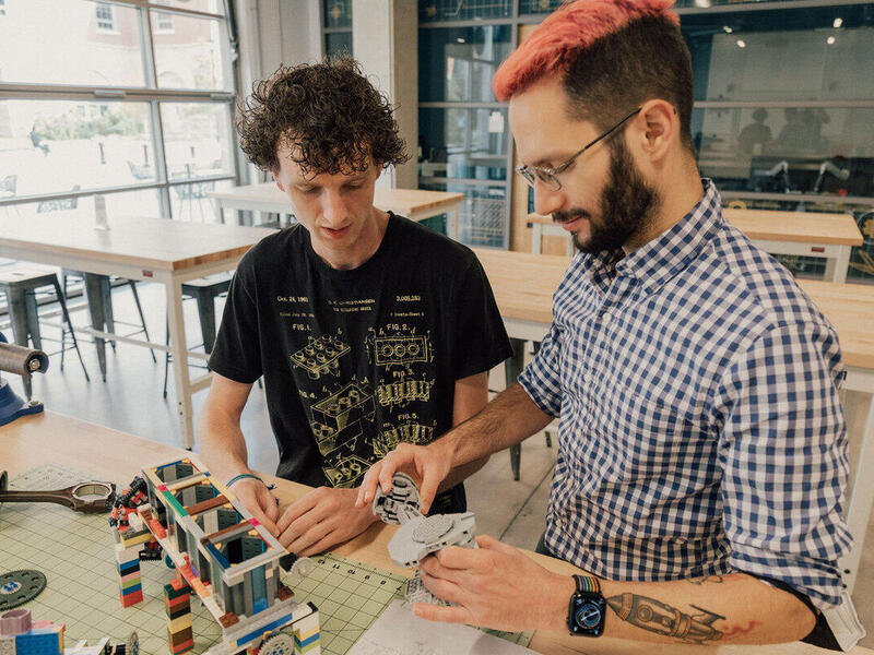 Two men sitting at a table building a lego structure 