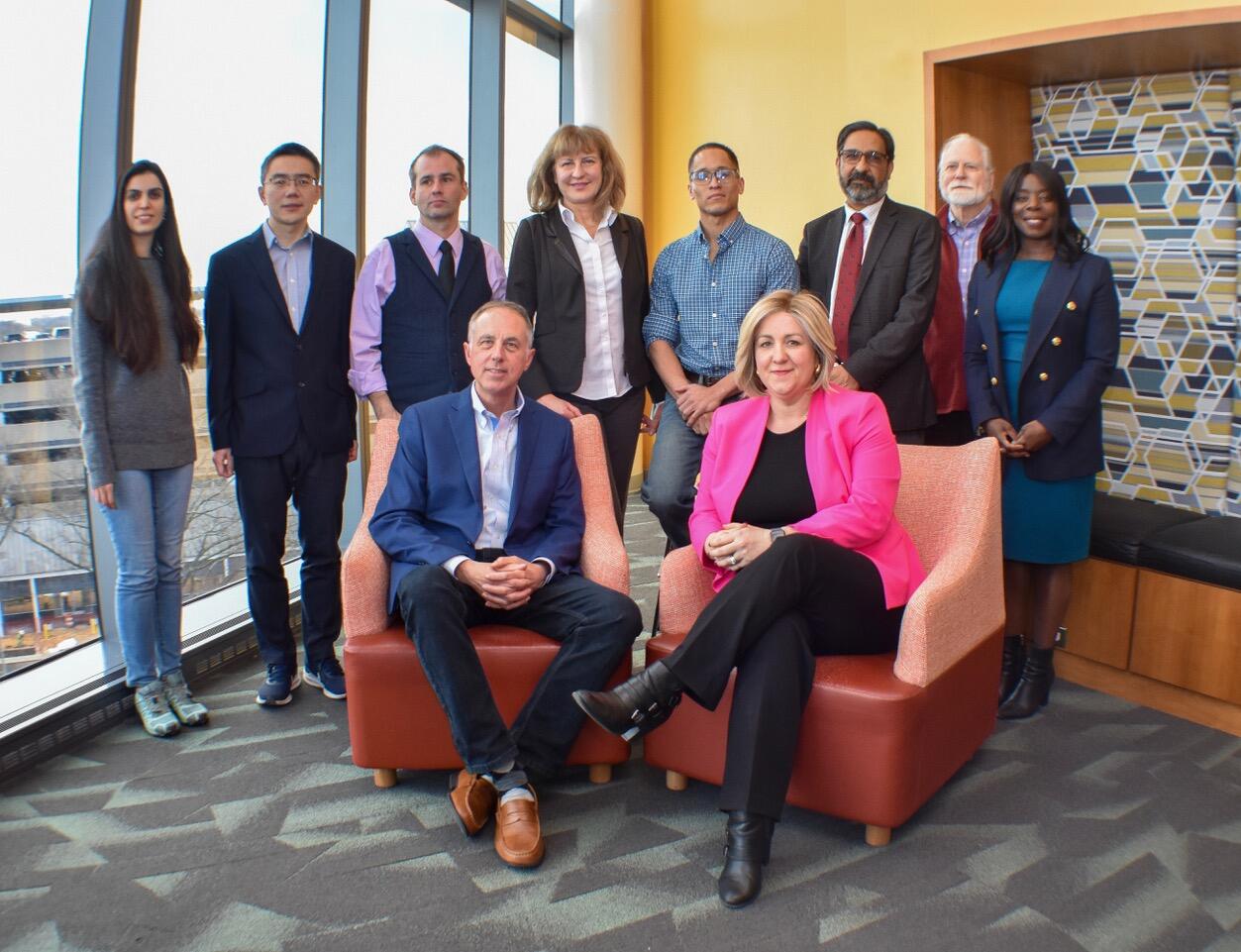A group photo of 10 people. A man and woman are sitting in two chairs in front of the other eight people who are standing behind them. 