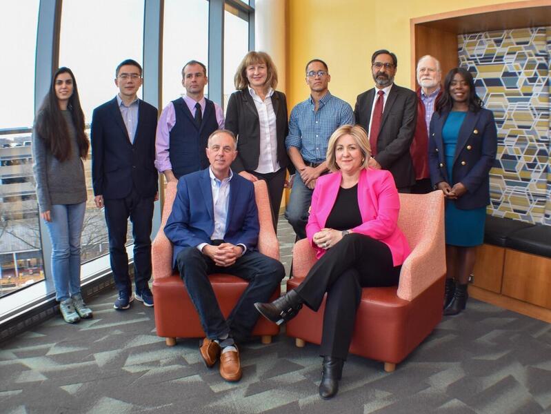 A group photo of 10 people. A man and woman are sitting in two chairs in front of the other eight people who are standing behind them. 