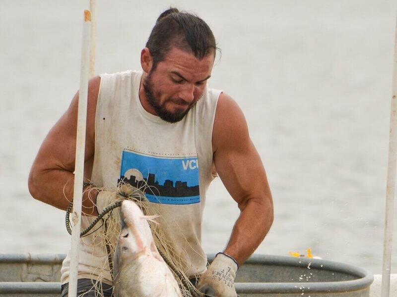 A photo of a man in a boat holding a large fish. 